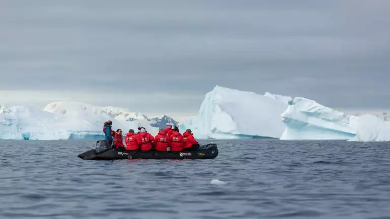 A zodiac filled with small cruise ship guests in red jackets exploring around icebergs and icy waterways