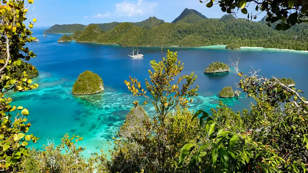 looking down at a beautiful desolate indonesia cove with a small ship anchored in the middle of it and jungle surrounding it.