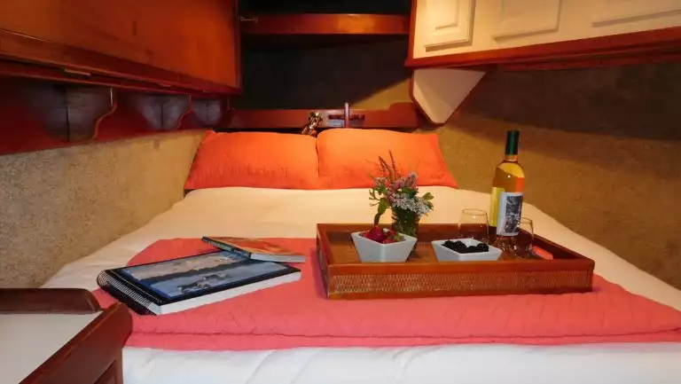 Guest cabin on Sikumi boat in Alaska with double bed in red & white linens with snack tray, upper & lower wood cabinets.