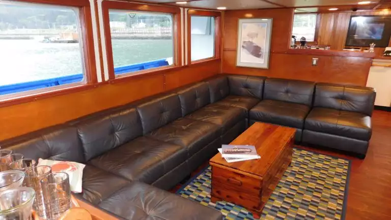 Large wraparound bench couch by wooden wall with view windows in lounge aboard Sikumi boat in Alaska.