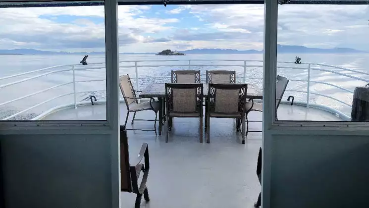 Aft exterior deck of Sikumi boat in Alaska with covered seating, wraparound white metal railing & ocean views.