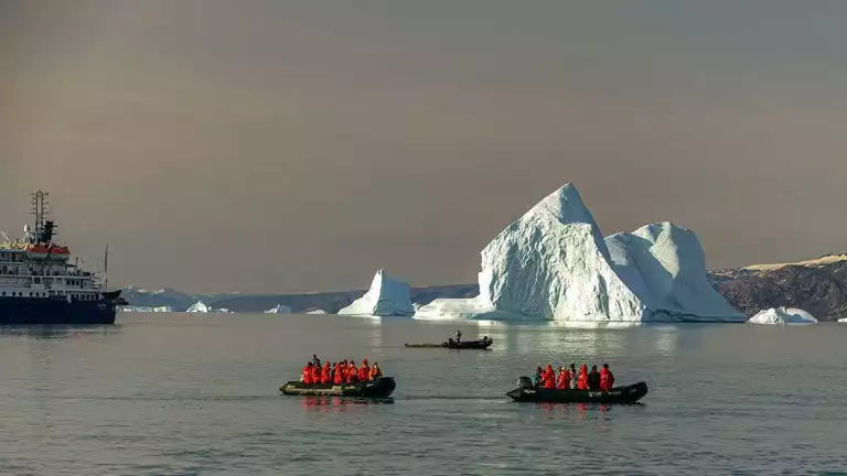 two zodiacs filled with travelers explore icebergs off a small cruise ship
