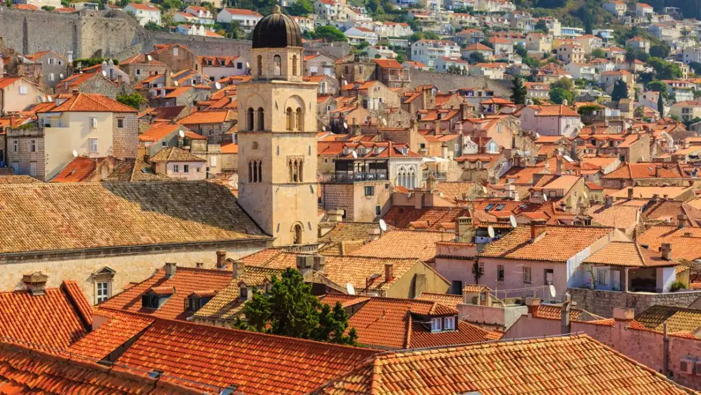 Aerial view of terracotta roofs & a belltower along the hilly old-world city of Dubrovnik, Croatia.