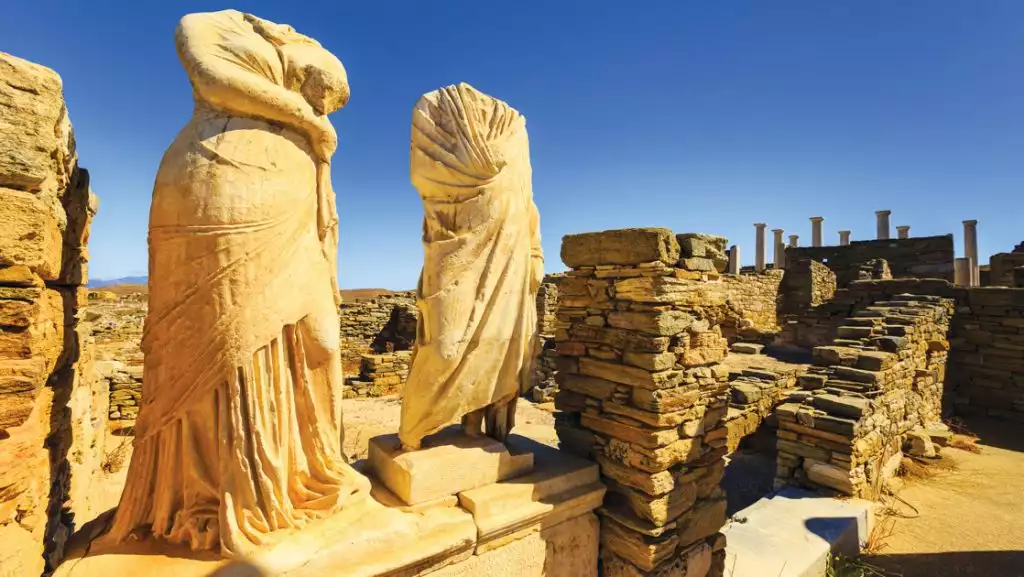 Headless male & female statues in Delos shine golden in sun during a Greece and Turkey cruise.