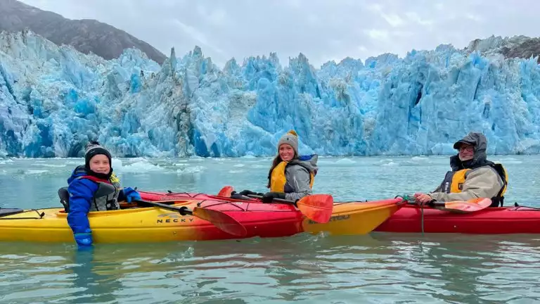 three Kayakers posing infront of the blue and white icebergs of alaska