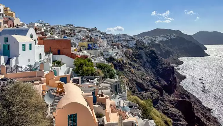 Cliffs of Santorini with stone buildings of varying colors overlooking brightly lit sea, seen on a Greek Isles Odyssey cruise.