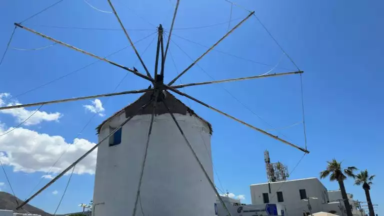 Simple windmill with long wooden arms tied to a round white building with a thatched roof, seen on the Greek Isles Odyssey cruise.
