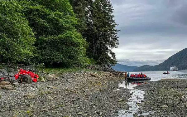 Travelers on a Lindblad Alaska cruise reach rocky beach in a Zodiac boat as more follow from small ship sitting in a remote cove.