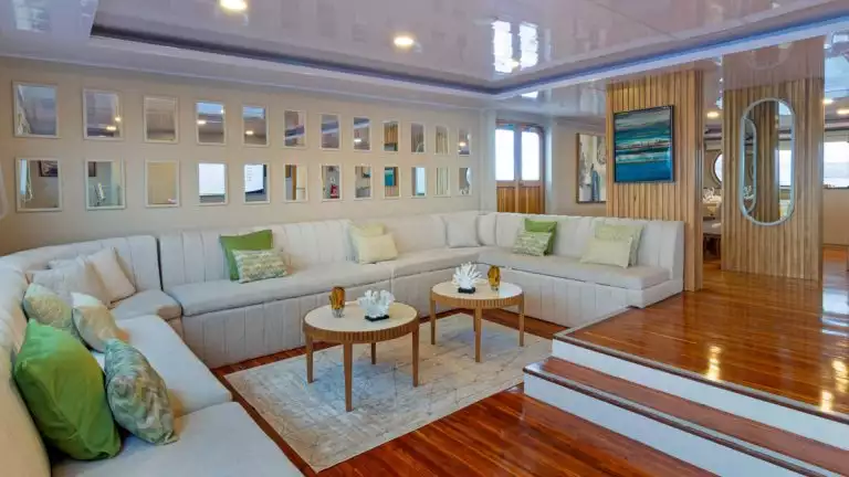 Living area on Petrel boat in Galapagos with sunken wood floor, wraparound beige couch with throw pillows & panoramic windows.
