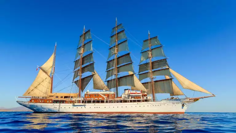 Wooden Windjammer sailing ship Sea Cloud with white hull & all sails unfurled sits on anchor above deep blue sea in Croatia.