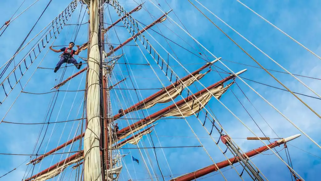 Crew in the rigging with sails rolled up on the ship Sea Cloud sailing ship under blue skies in the Mediterranean.
