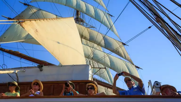Guests take photos from the ship Sea Cloud at full sail under clear blue skies in the Mediterranean.