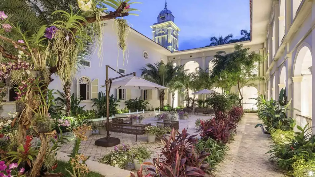Courtyard of luxury Hotel del Parque in Guayaquil, Ecuador, with lush plants in bloom, stone floor & view to belltower.