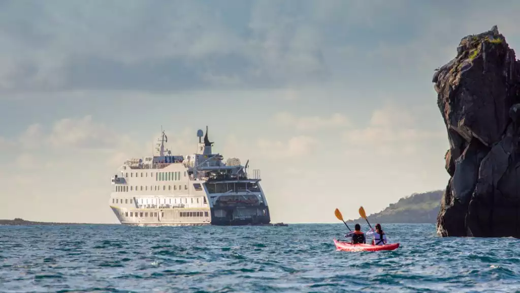 Guests kayaking near the ship National Geographic Endeavour II in open waters near cliffy rocks