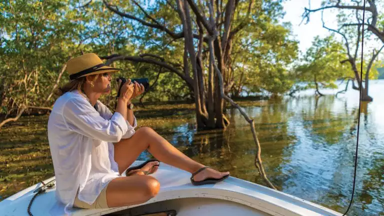 Women in white shirt and tan hat photographing off a small boat