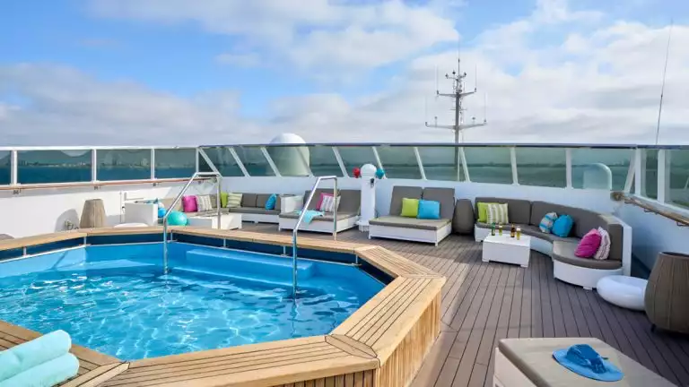 Sun Deck on Nat Geo Islander II ship in Galapagos with large Jacuzzi & many gray chaise loungers with colored throw pillows.