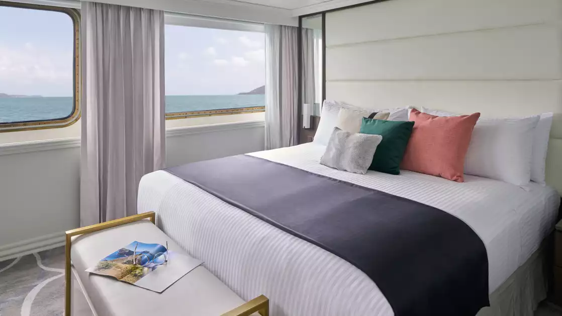 Suite aboard National Geographic Islander II Galapagos ship with double bed, large view windows & white & blue decor.