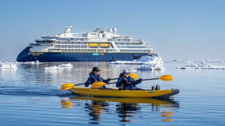 Kayakers explore the icy waters off the national geographic expedition ship ship that is shown behind them.