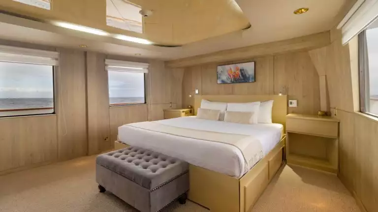 Master Suite with white bedding in light tan room with king bed aboard small cruise ship