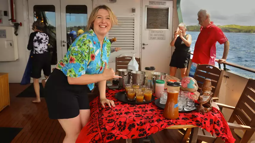 Crew of small cruise ship posing for a photo in a hawaiian shirt in front of drinks