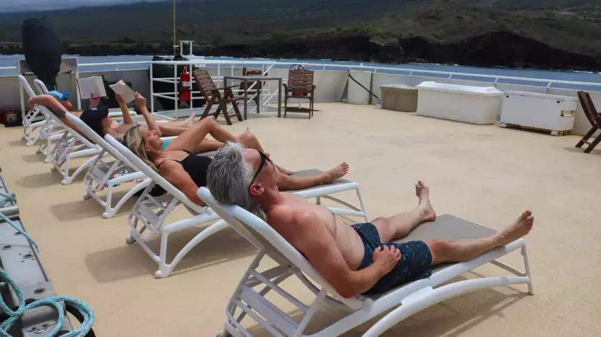 Guests lay out on the sun deck tanning and reading infront of the Hawaiian islands. 