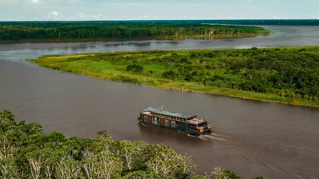 The Aqua Nera cruise ship seen from an aerial shot among a winding Amazon River with bright green trees and bushes along the riverbank