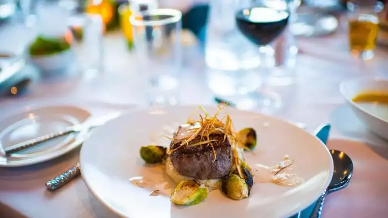 A steak dinner beautifully plated with brussel sprouts on a white place setting