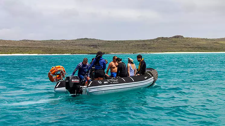 Galapagos Angel cruise passengers seen in a skiff in aqua blue water near a deserted shore