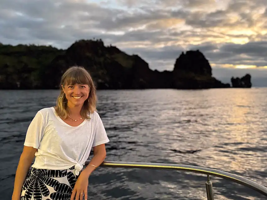 A woman in a white shirt smiles and leans on the railing of a ship in the Galapagos Islands
