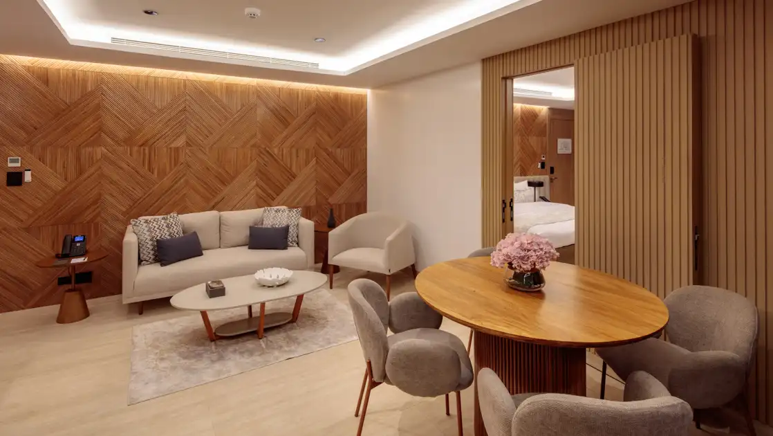 Second room of Owner's Suite with tan couch & wood table with beige chairs & pink flowers on Hermes Galapagos mega catamaran.