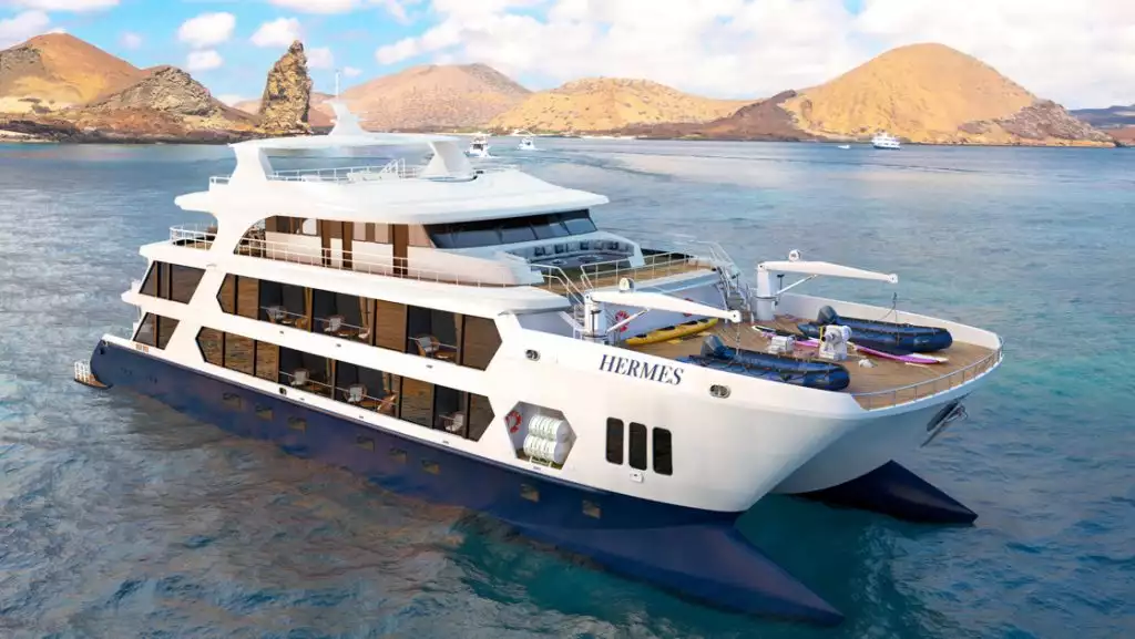 Rendering of Hermes mega-catamaran sitting offshore in the Galapagos with 4 guest decks, blue hulls & white exterior.