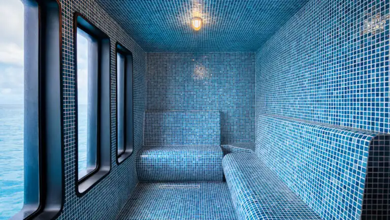 Blue tile steam room with bench seating, oval windows & silver shower wands on Hermes ship in Galapagos.