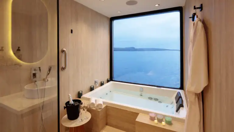 Guest bathroom with stone tub by window, glass-walled rain shower, vanity & dual bowl sinks on Hermes Galapagos catamaran.
