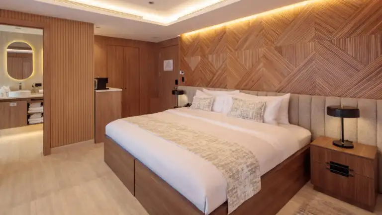 Double Suite with king bed on Hermes mega catamaran with white linens, modern furniture, wood accent walls & recessed lighting.