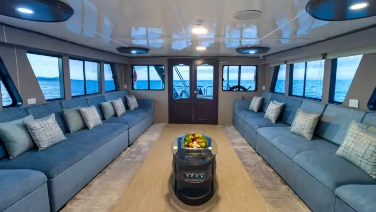 2 long rows of padded blue couches face each other with a small glass coffee table in between & view windows on Monserrat boat.