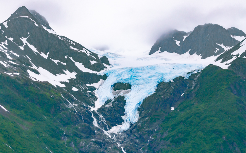 Glaciers fill the green and brown sharp snowy mountains waterfalling down the front.