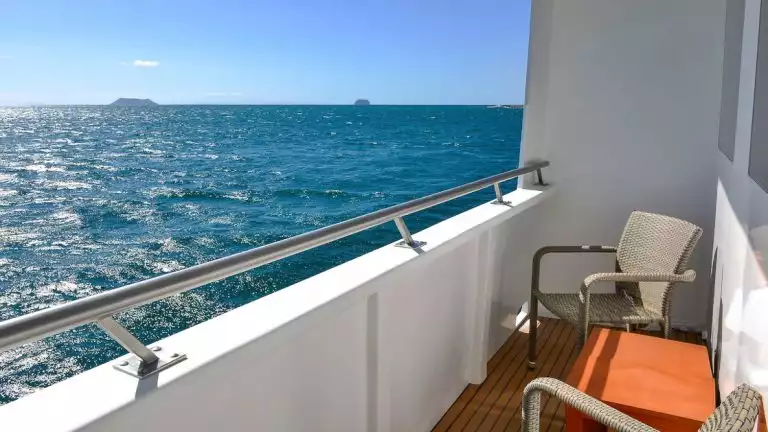 Balcony from Category 5 Cabin aboard National Geographic Delfina with two whicker chairs, coffee table, and views of Galapagos.