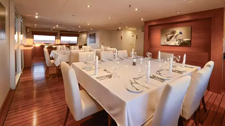 Dining room aboard Galapagos catamaran National Geographic Delfina two square tables with white table cloth, white fabric chairs.