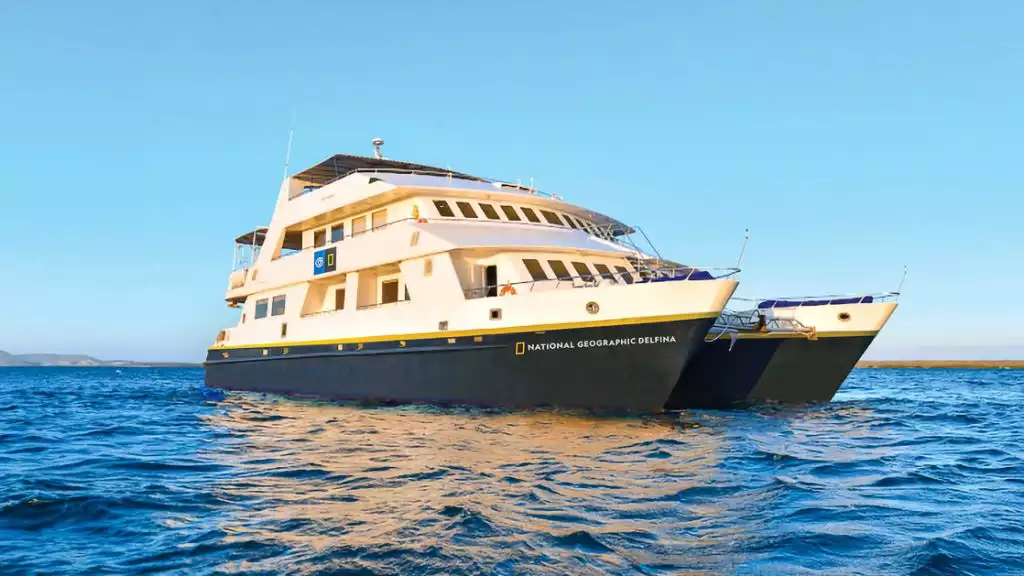 Luxury catamaran National Geographic Delfina. Colored white with a royal blue hull floats in the Galapagos on a blue sunny day