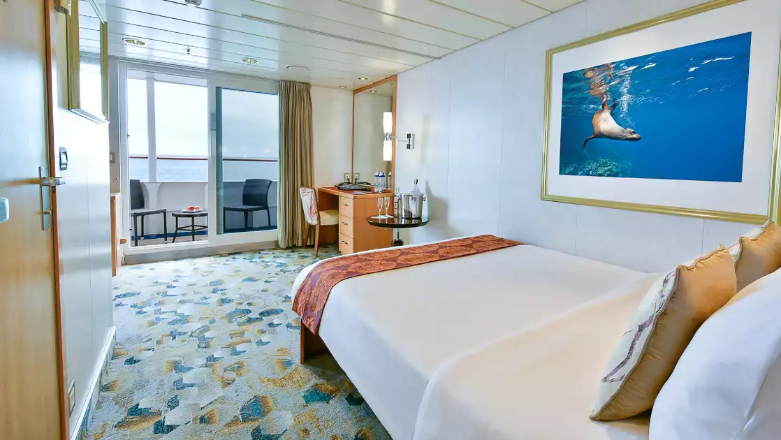 Floor to ceiling glass door to balcony with single bed of white bedding, white walls and large framed photo, vanity desk and mirror.