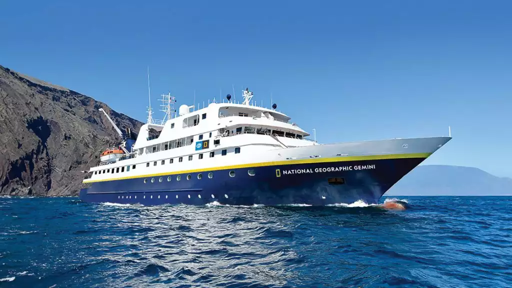 Exterior of Nat Geo Gemini, painted white with navy blue hull and floating in the ocean in blue sky day in Galapagos.