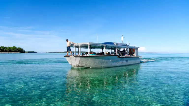 Xplorer tender vessel with silver hull & open-air, shaded seating area motors through turquoise sea in Indonesia.