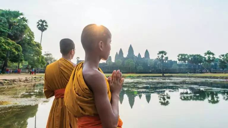 Two young monks at Angkor Wat, temple complex, in Cambodia overlooking calm waters and green trees