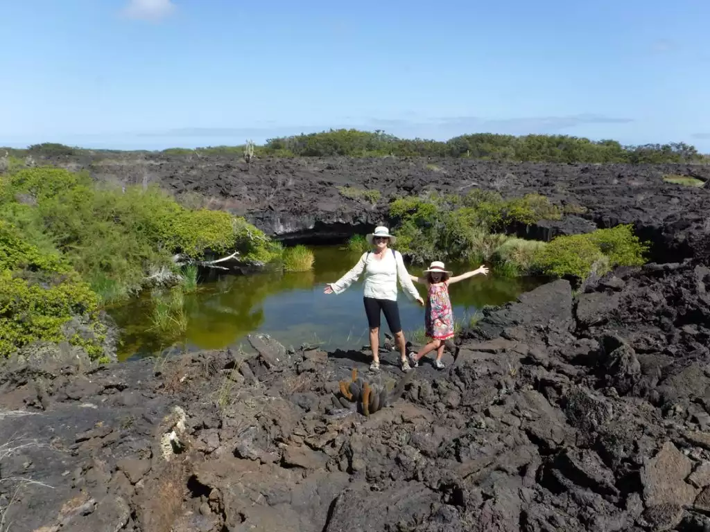 A mother and daughter pose arms up on lava rock by a small pond in Galapagos