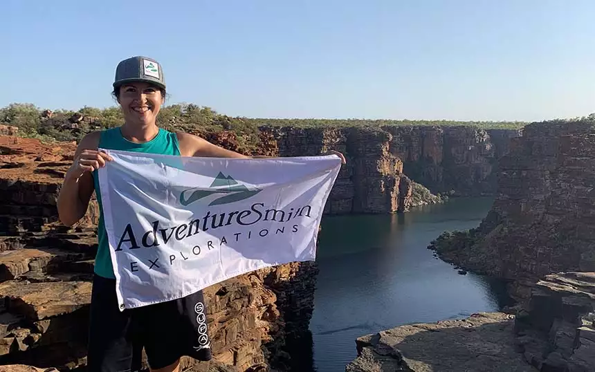 A traveler in a hat holds an AdventureSmith flag overlooking cliffs from a Kimberley Australia cruise