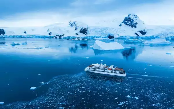 Operating Antarctica cruises the futuristic all white Greg Mortimer plys the blue ocean near icebergs and snowy mountain landscapes.
