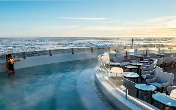 Woman in black bathing suit stands in heated outdoor pool on top deck of expedition ship on a luxury Antarctica cruise.