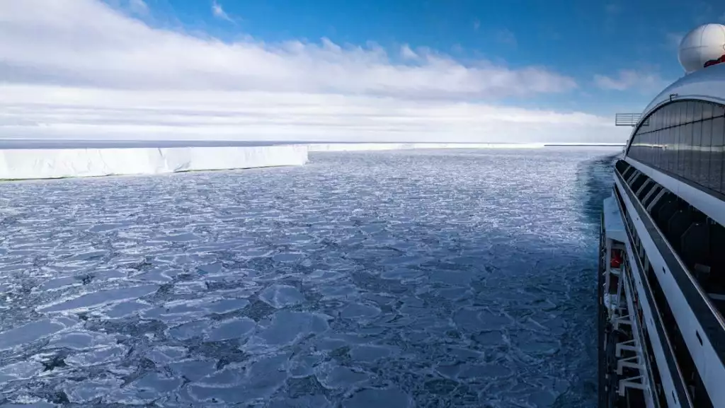 Starboard side of Le Commandant Charcot small ship as she crushes through pack ice while cruising along a big tabular iceberg.