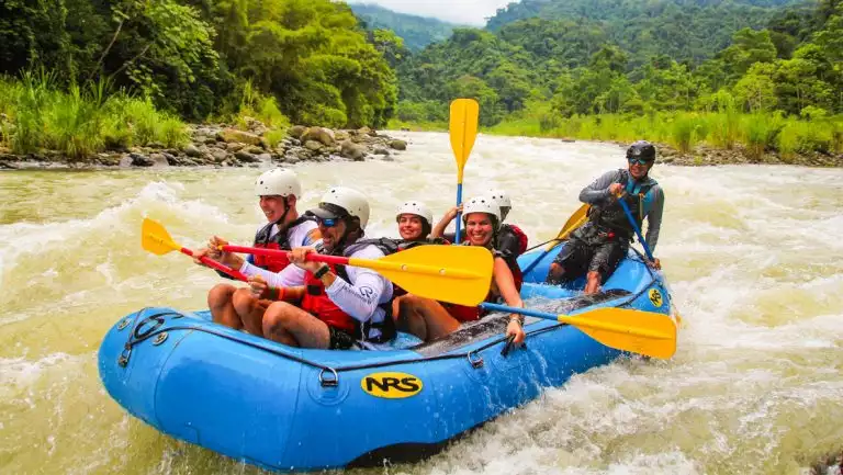 Kontiki Pura Vida Expedition Cruise guests paddle an inflatable blue raft through whitewater rapids beside bright green jungle.