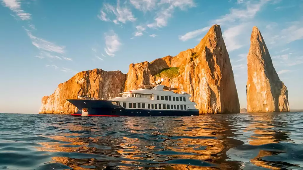 A Galapagos luxury yacht seen in front of Kicker Rock at golden hour